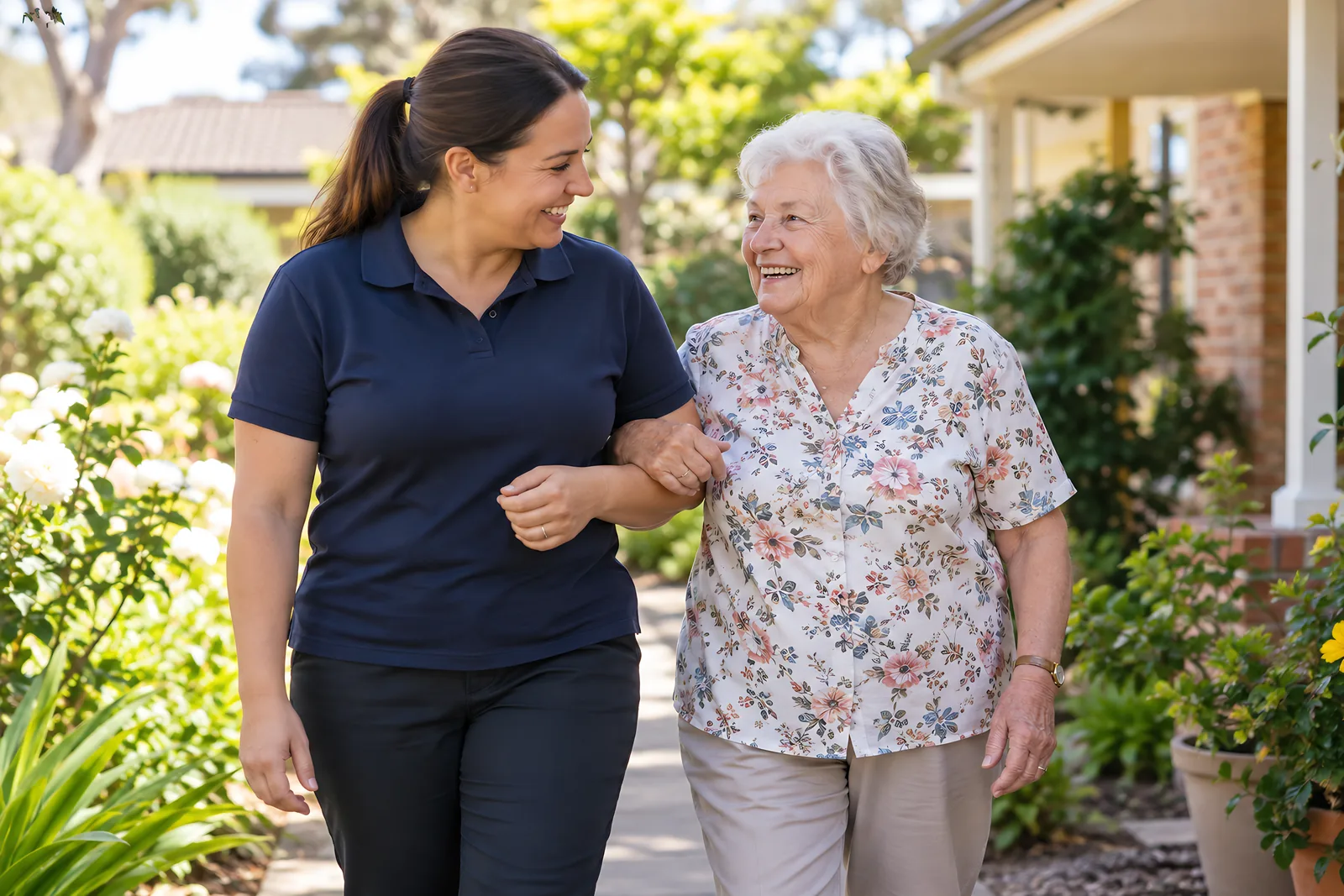 Support worker walking arm in arm with an older woman along a garden path
